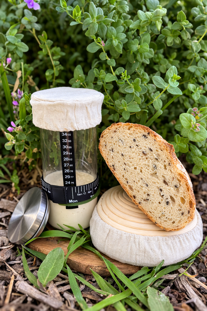 Bread and a container of starter on a wooden board with greenery in the background
